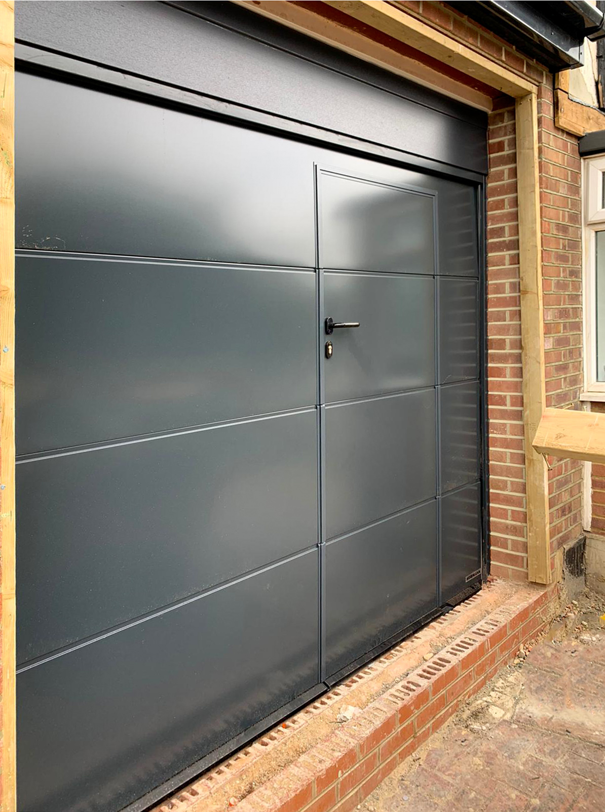 A Hormann LPU42 L-Ribbed Sectional Garage Door + Wicket Door finished in Anthracite Grey & Installed by our New Malden Branch.