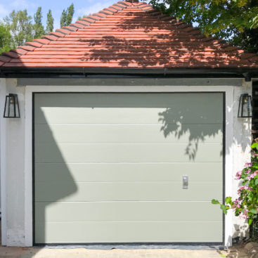 An SWS SeceuroGlide Elite Garage Door finished in Farrow & Ball Pigeon between the opening in a white frame. It features manual operation with an aluminium handle